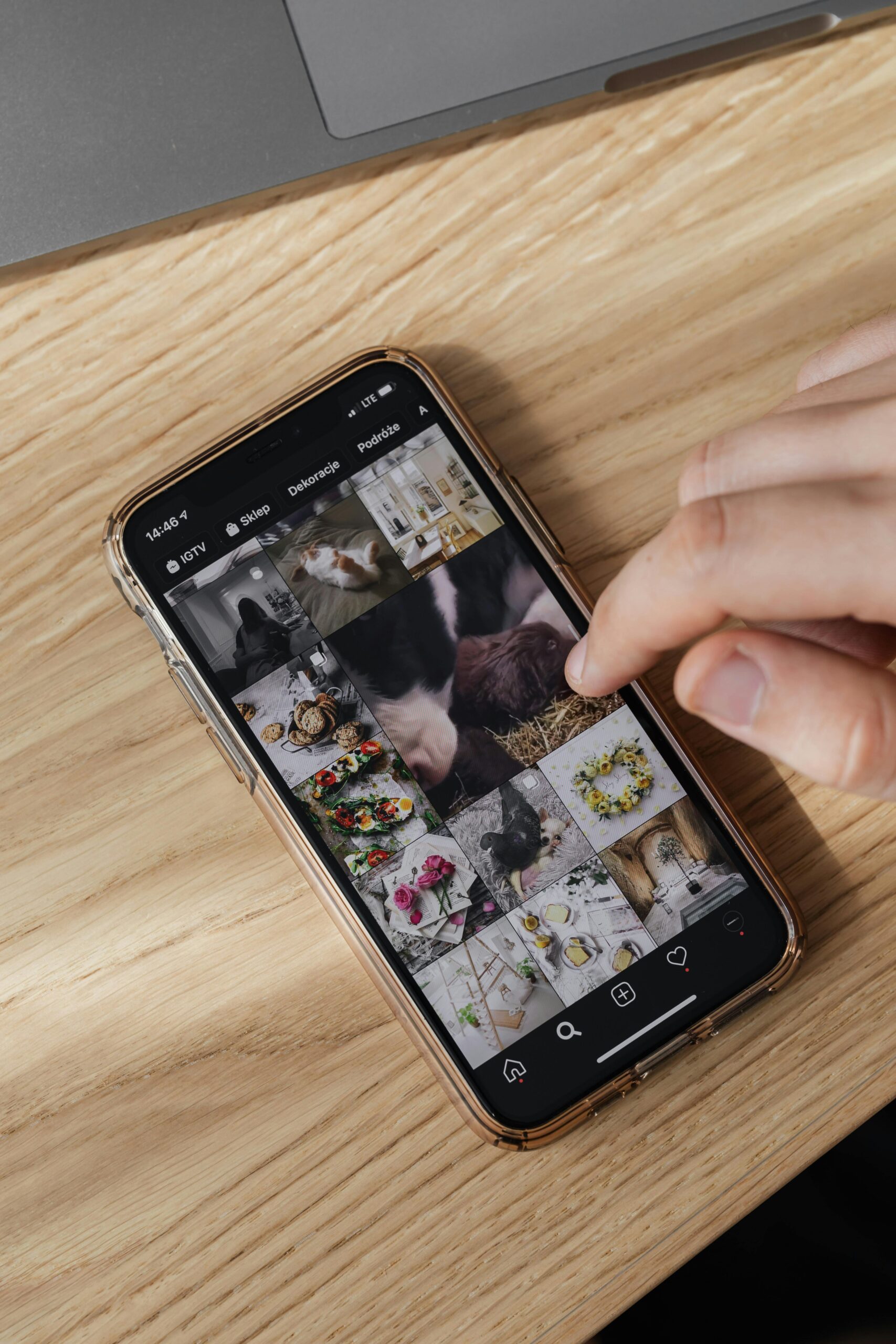 From above of crop unrecognizable person checking pictures in smartphone gallery and scrolling touchscreen cellphone on wooden table near laptop